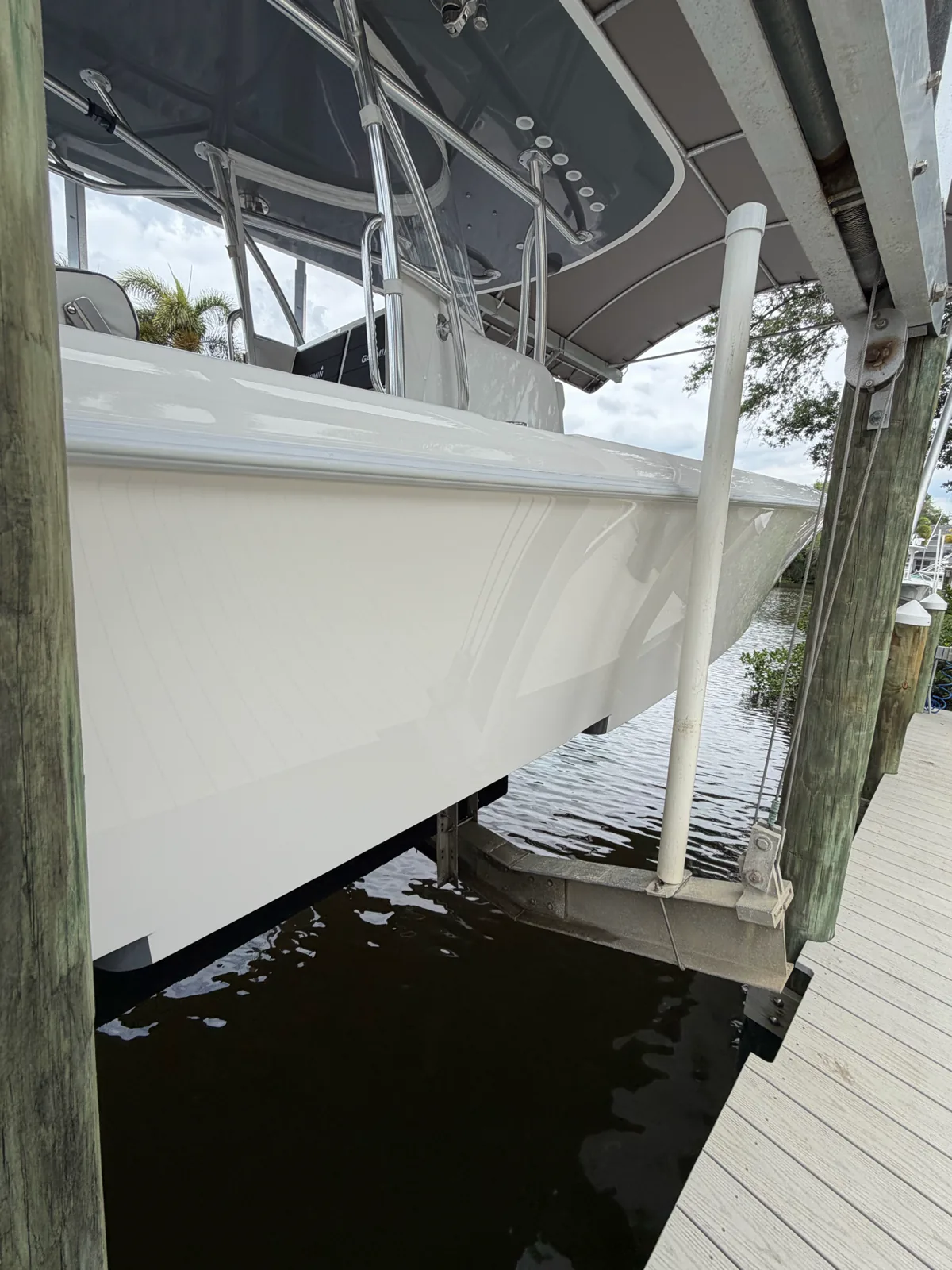 White boat hull on a lift above the water beside a wooden dock