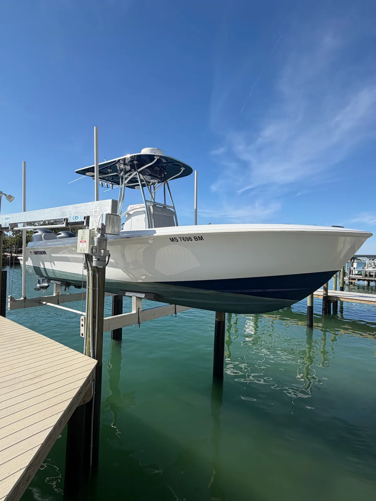 White center-console boat with a dark lower hull resting on a lift above the water