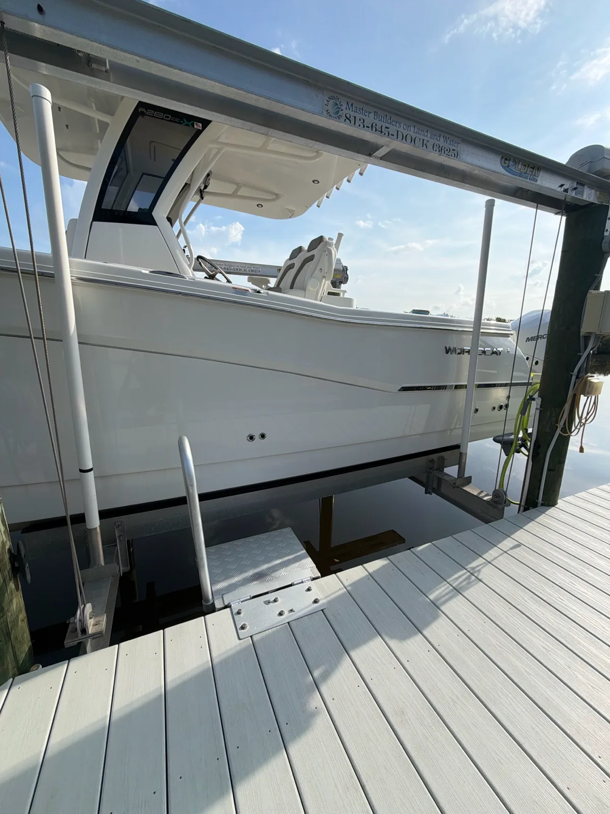 White boat suspended on a lift beside a wooden dock