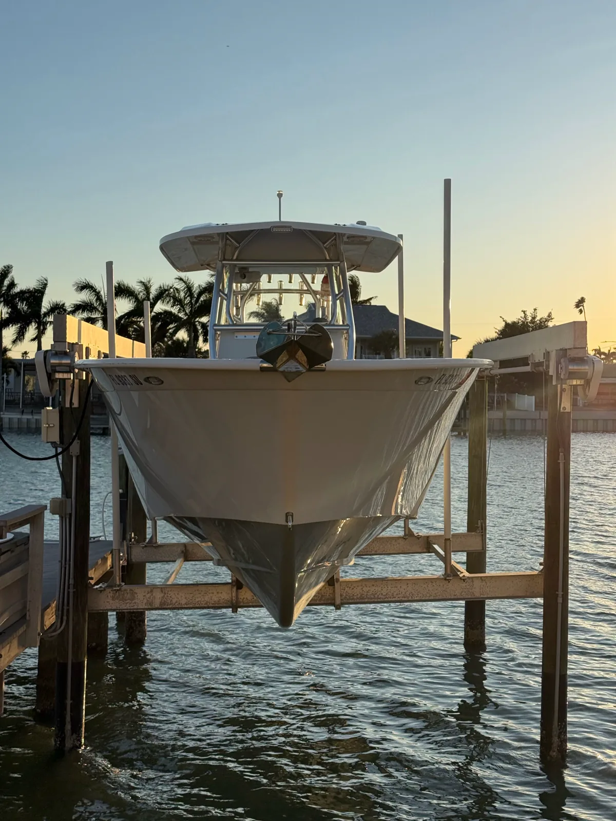 Front view of a white center-console boat suspended on a lift above the water