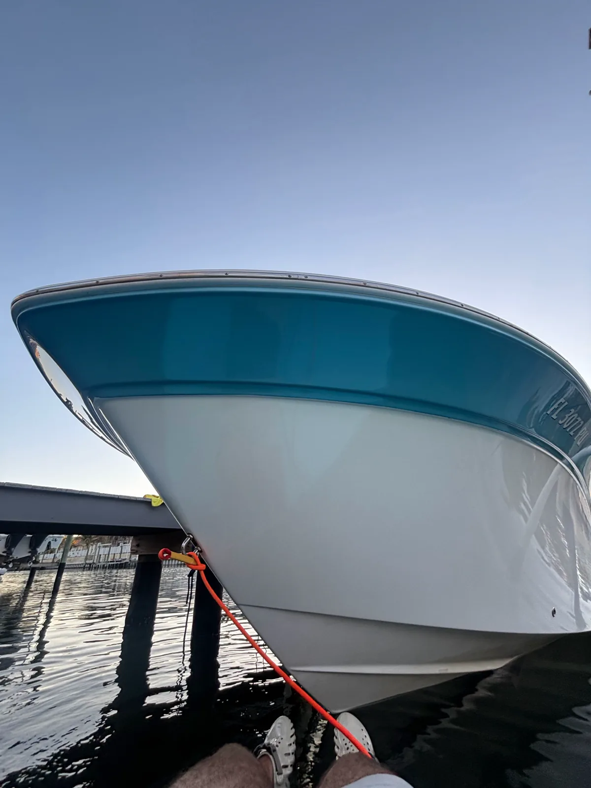 White and teal boat hull tied beside a wooden dock over the water