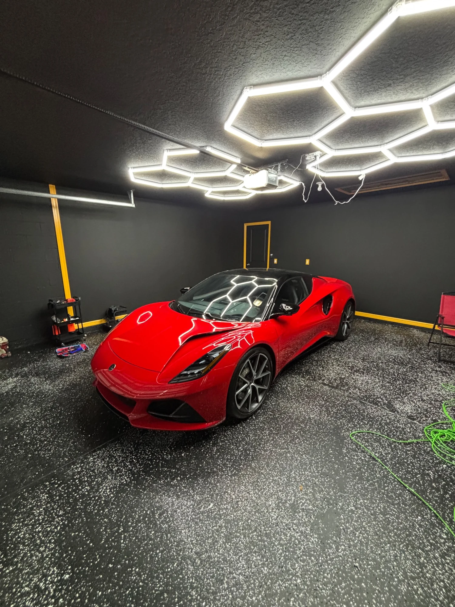 Red performance car displayed beneath inspection lighting inside a detailing workspace