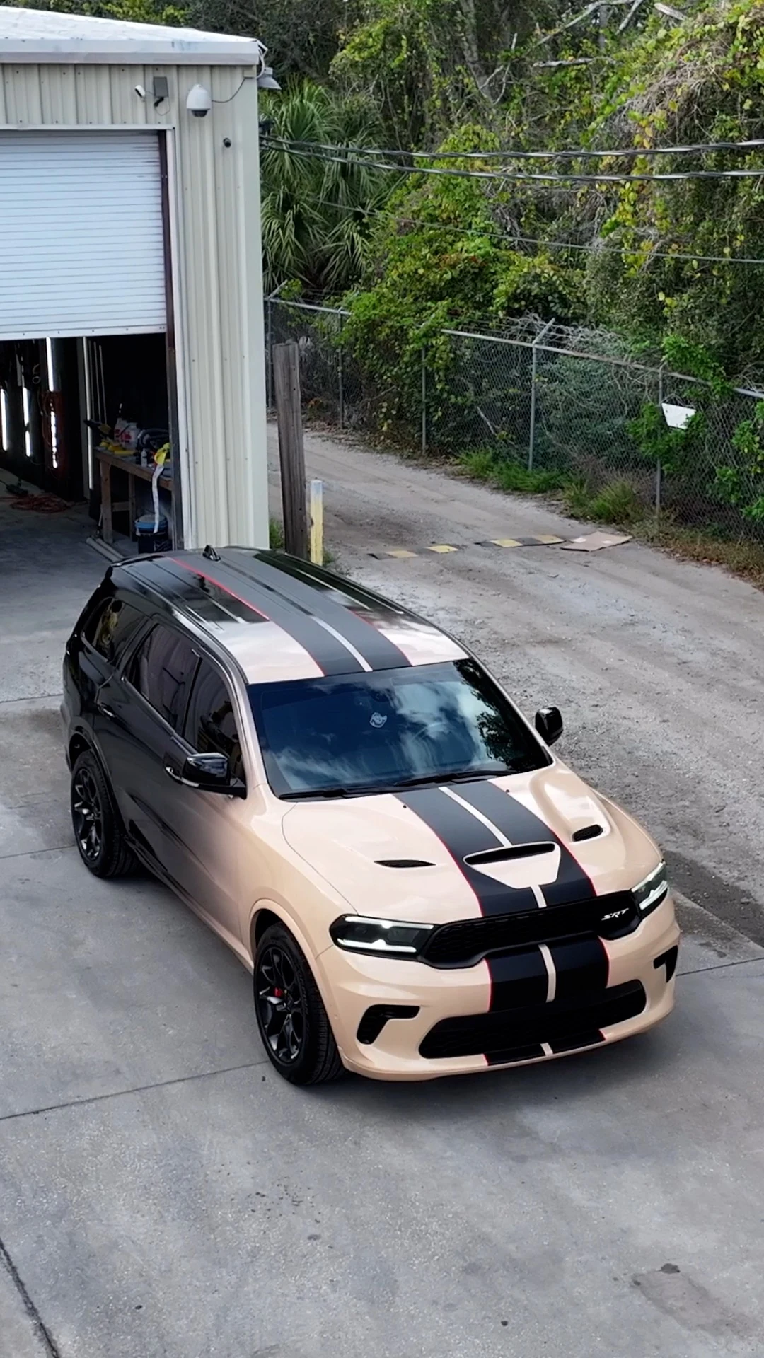 Light bronze Dodge Durango SRT with black center stripes photographed outside an automotive workspace