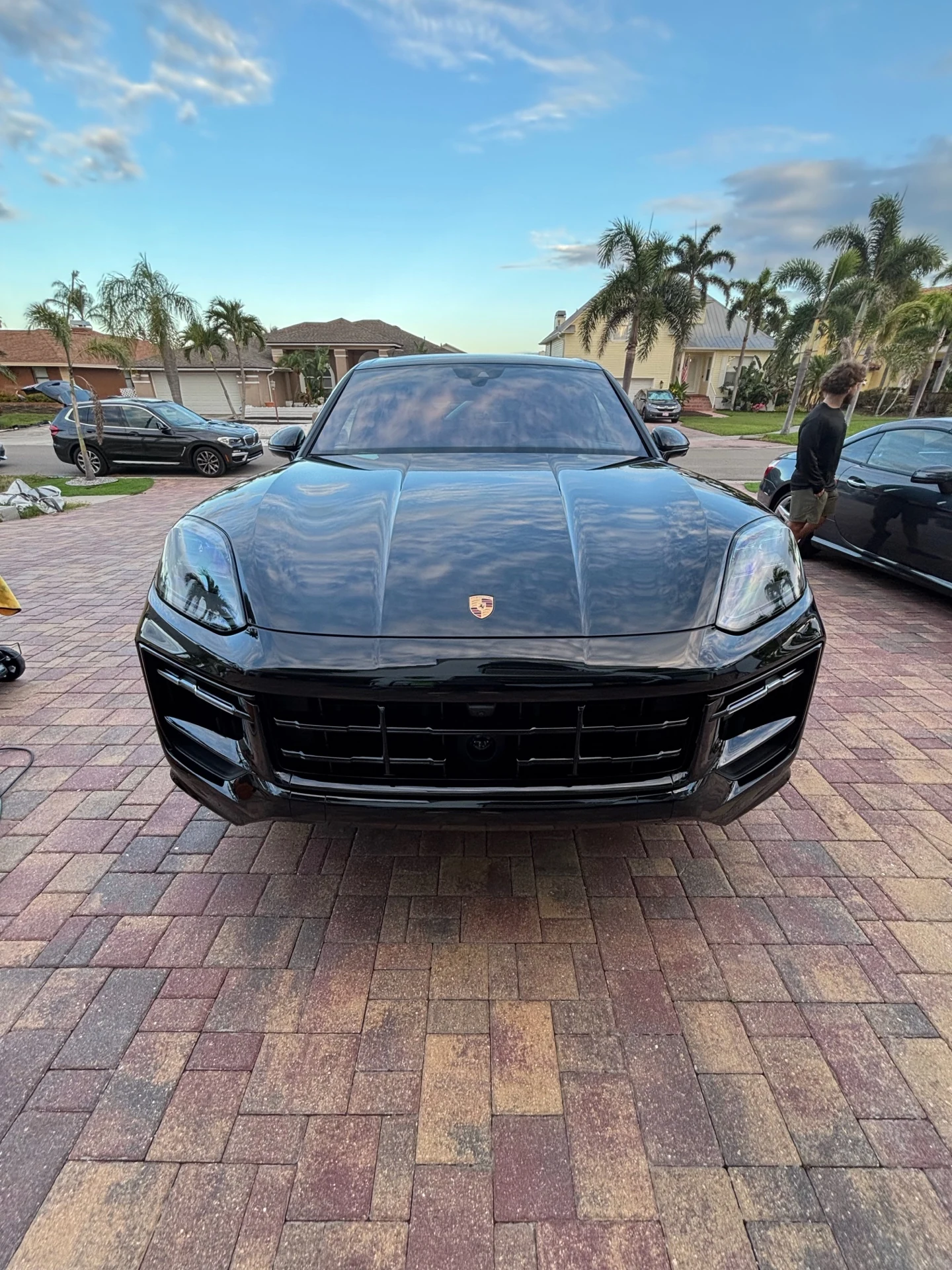 Black Porsche SUV photographed from the front with clear sky reflections across the hood